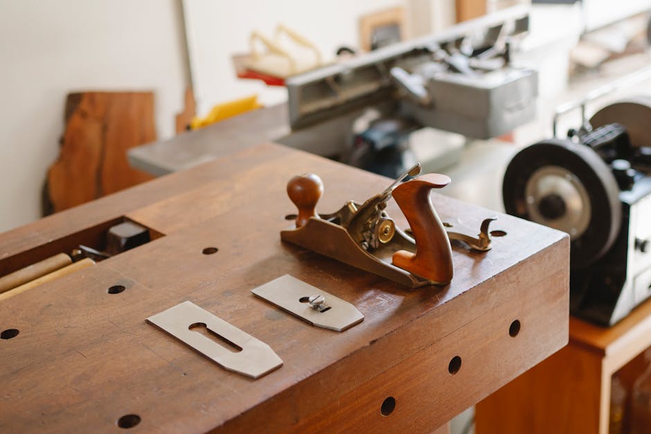Professional jointer with collection of metal knives placed on wooden table in workshop with special metal machines on blurred background