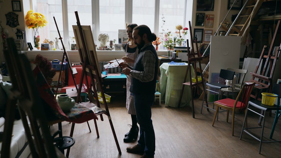 Two artists painting together in a bright, sunlit studio filled with art supplies and vibrant colors.