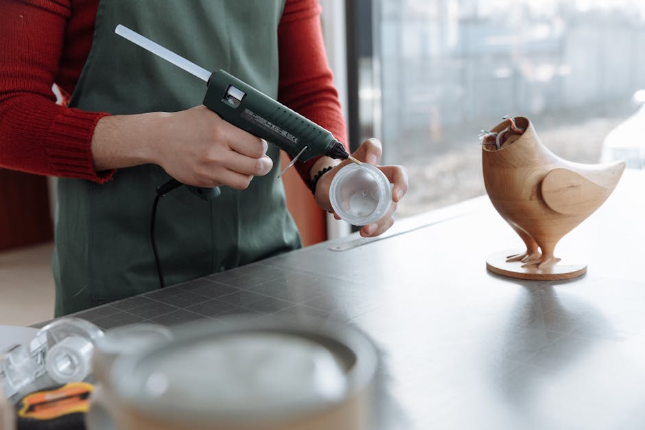 A person using a glue gun to assemble a wooden toy bird, showcasing craftsmanship.